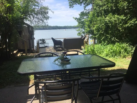 Sunny patio with a glass dining table and chairs overlooking the water and a dock