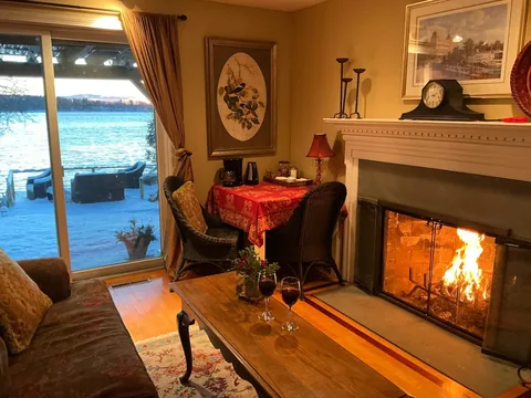Cozy living room with a lit fireplace, wine glasses, and a view of the deck through the window